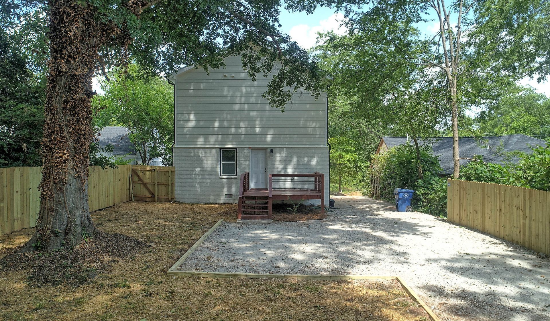 Backyard with wooden fence, gravel area, small deck, and a two-story house.