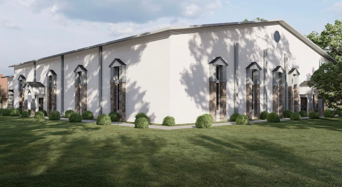 White building with arched windows, surrounded by green grass and trees.