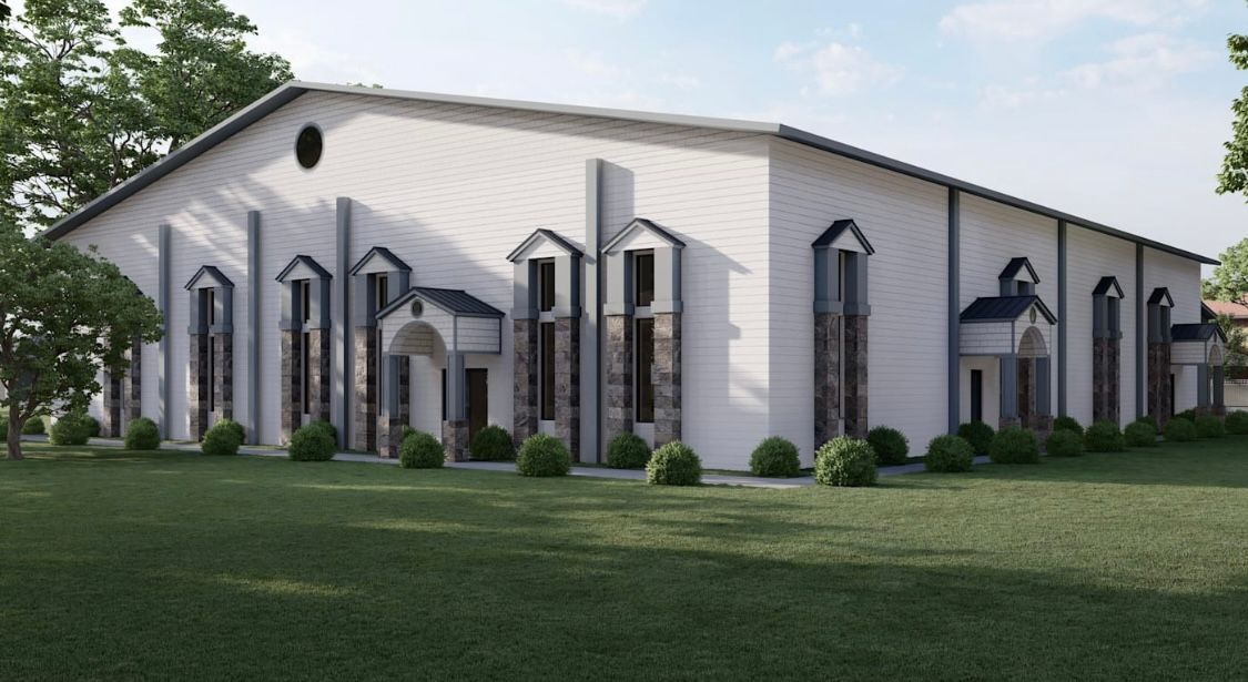 White building with tall windows and arched doorways, green lawn and trees.
