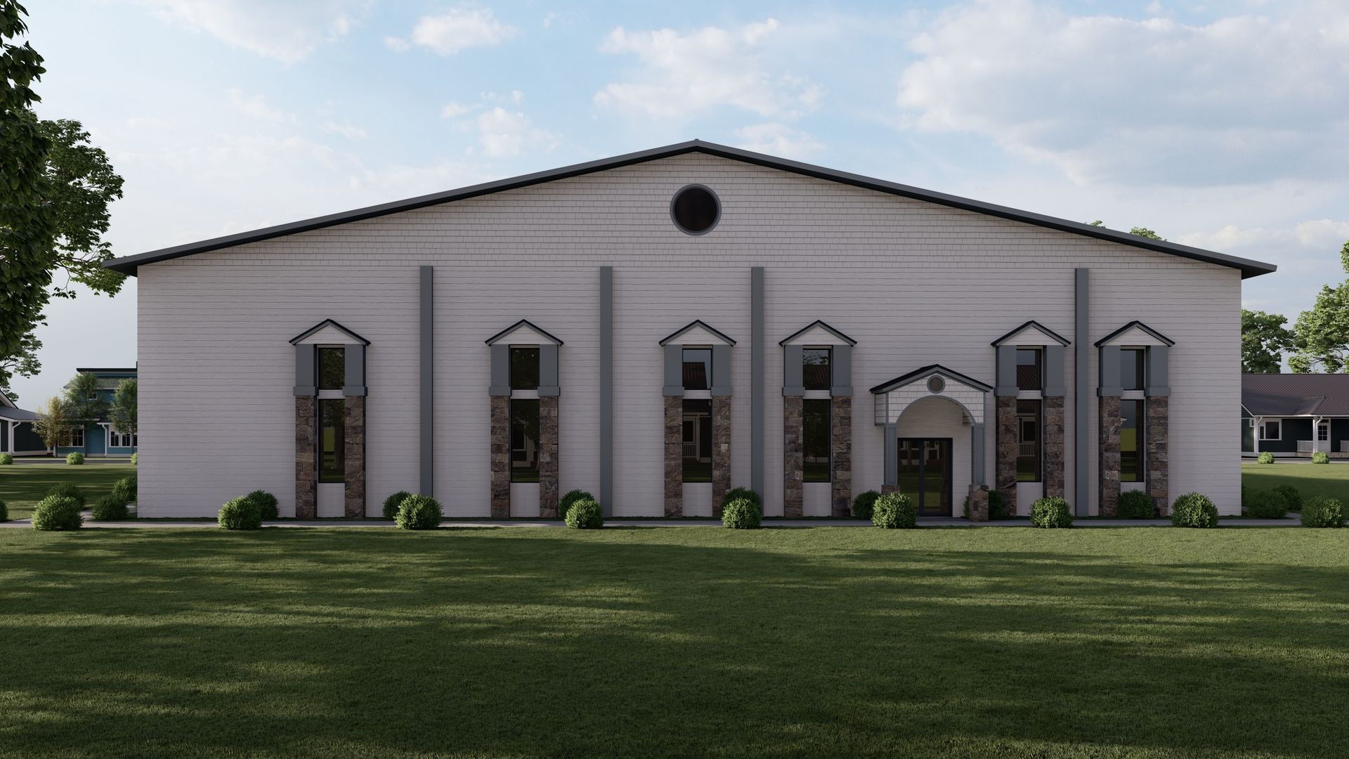 White building with a dark roof and decorative windows, set on a green lawn with trees.