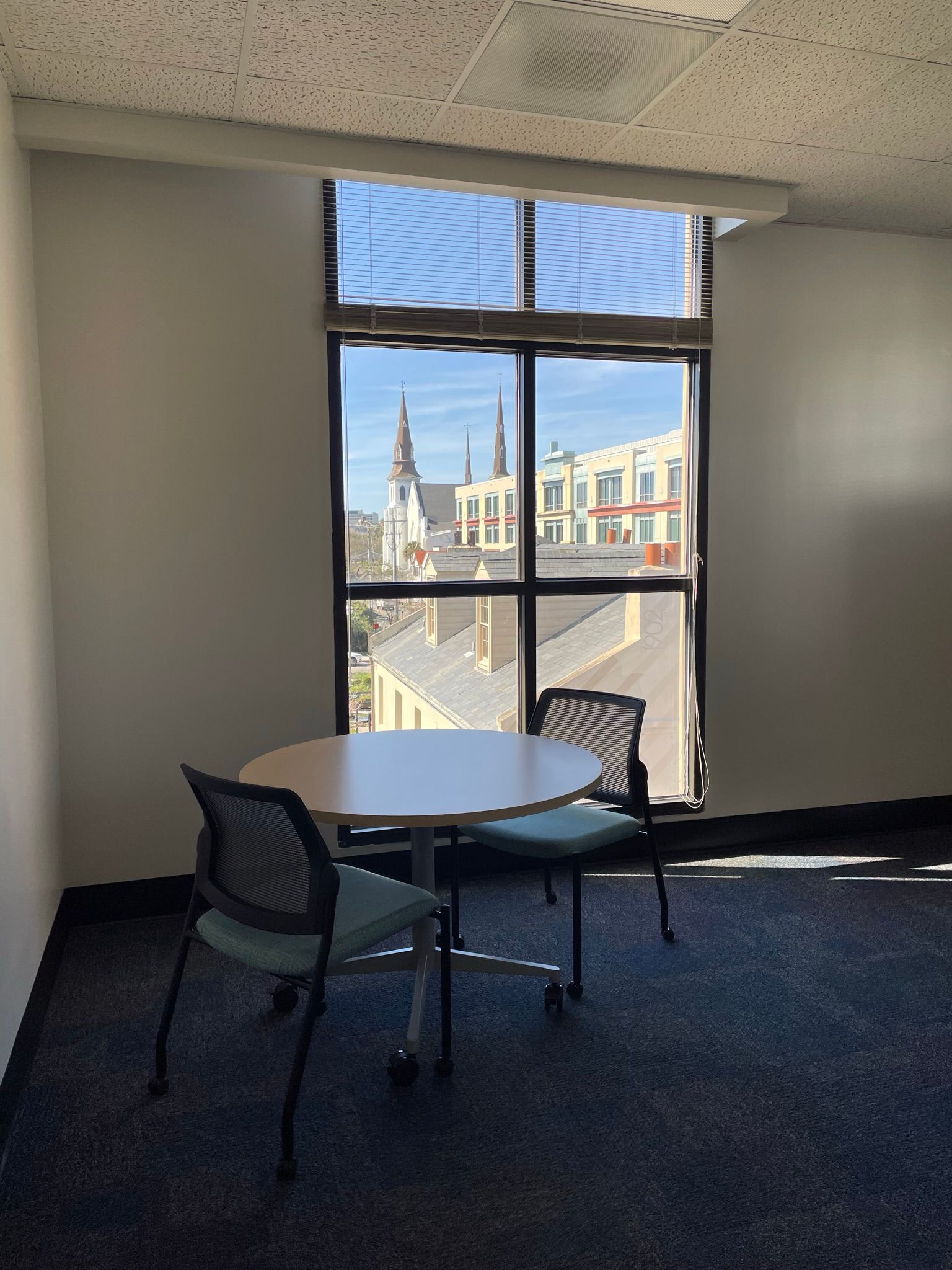 Round table with two chairs by a window in a room with a view of buildings.