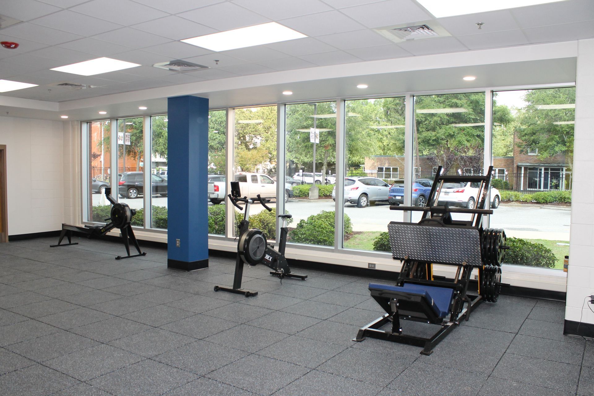 Gym with exercise equipment and large windows overlooking a street.