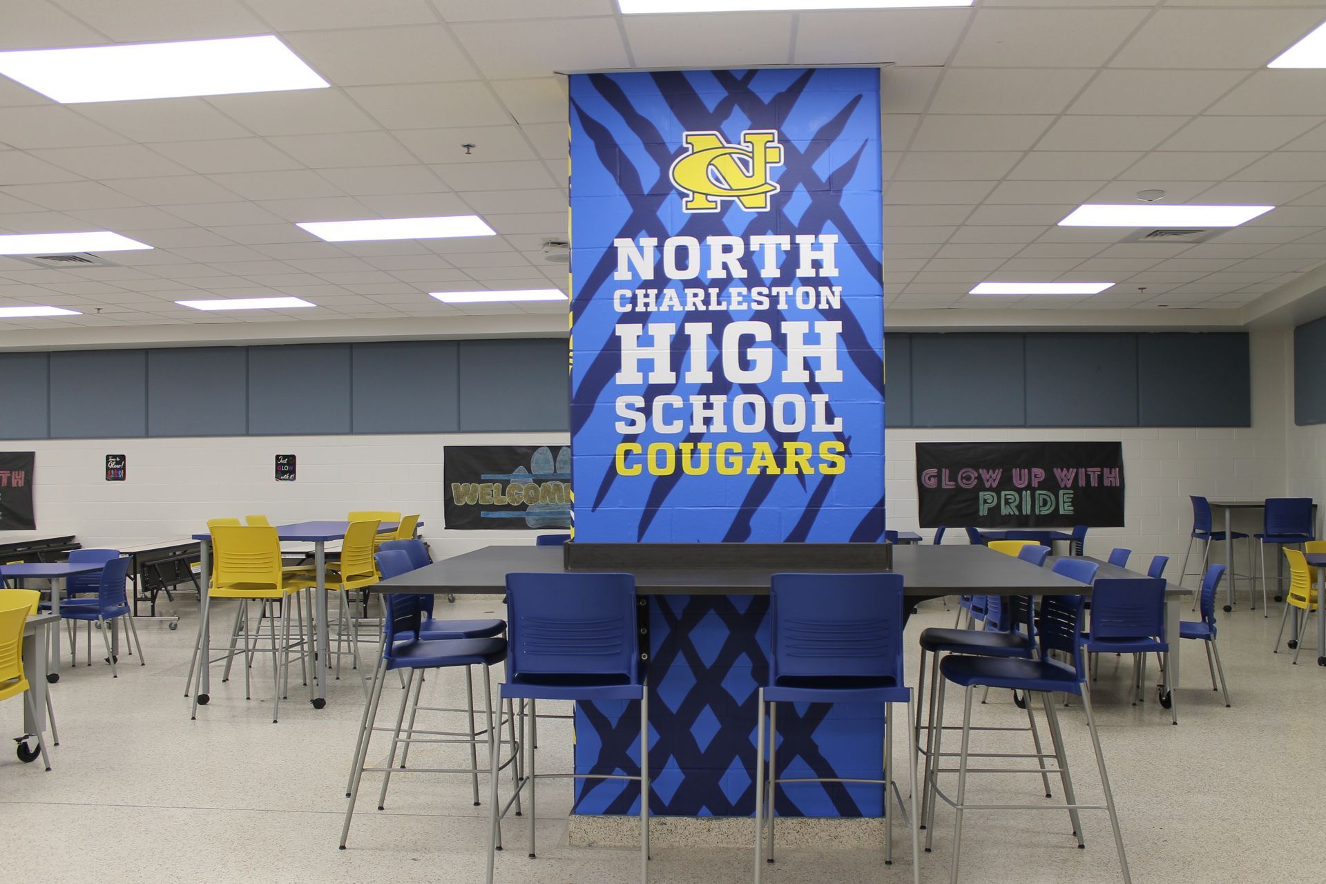 North Charleston High School cafeteria with a banner and tables. Blue, yellow, and white colors.