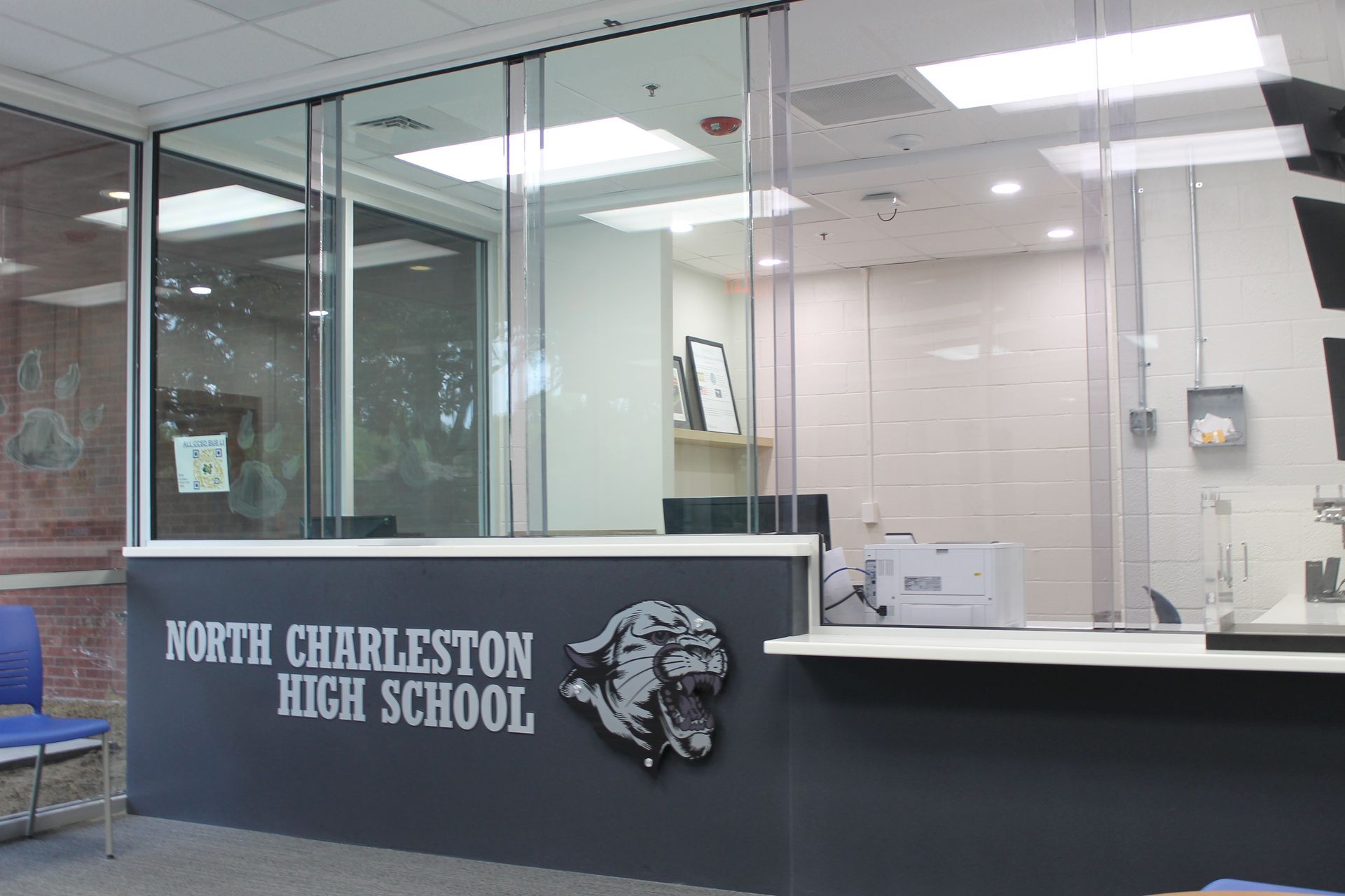 North Charleston High School reception area with a school logo, clear glass barrier, and desk.