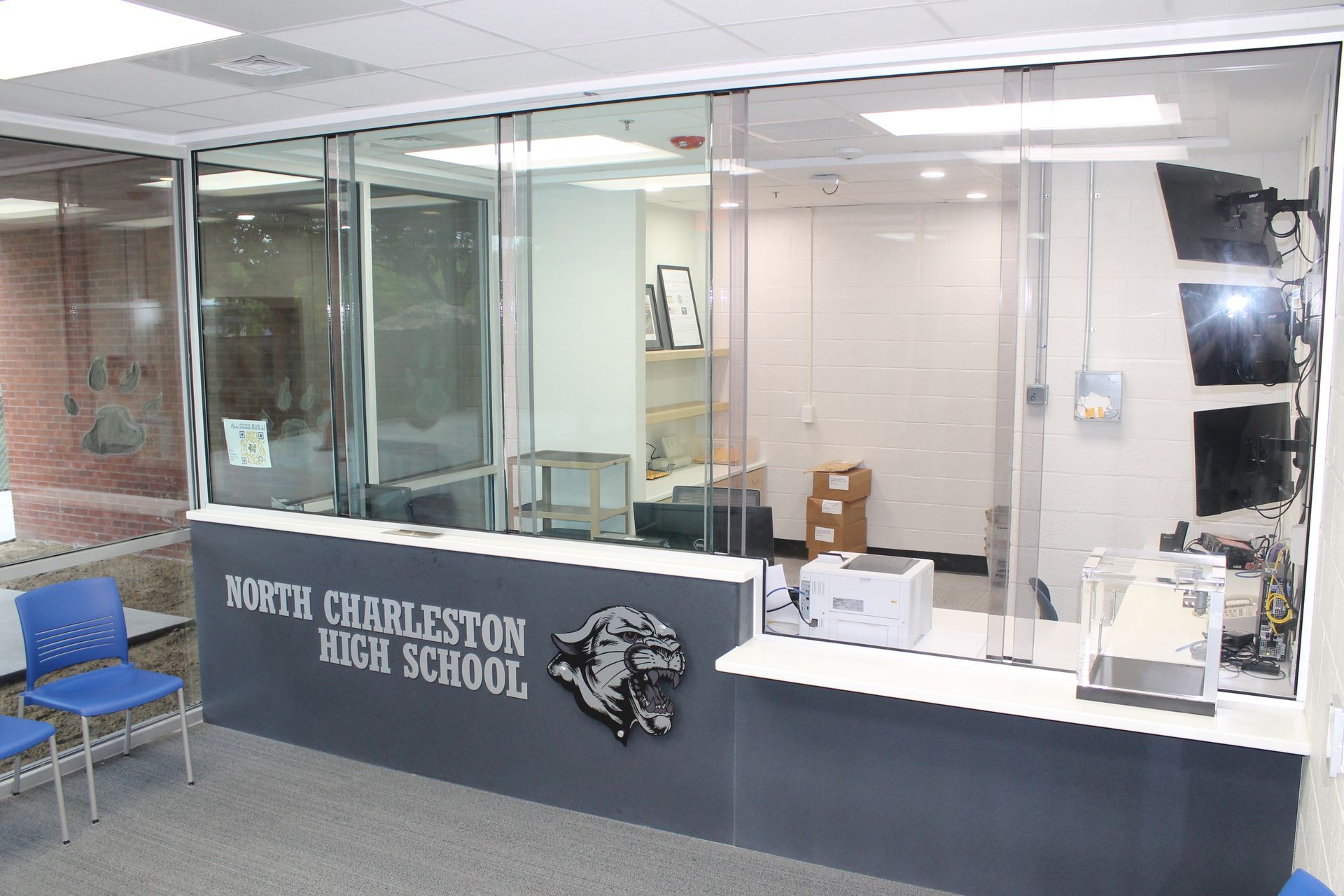Reception desk at North Charleston High School with glass barriers and a school logo.