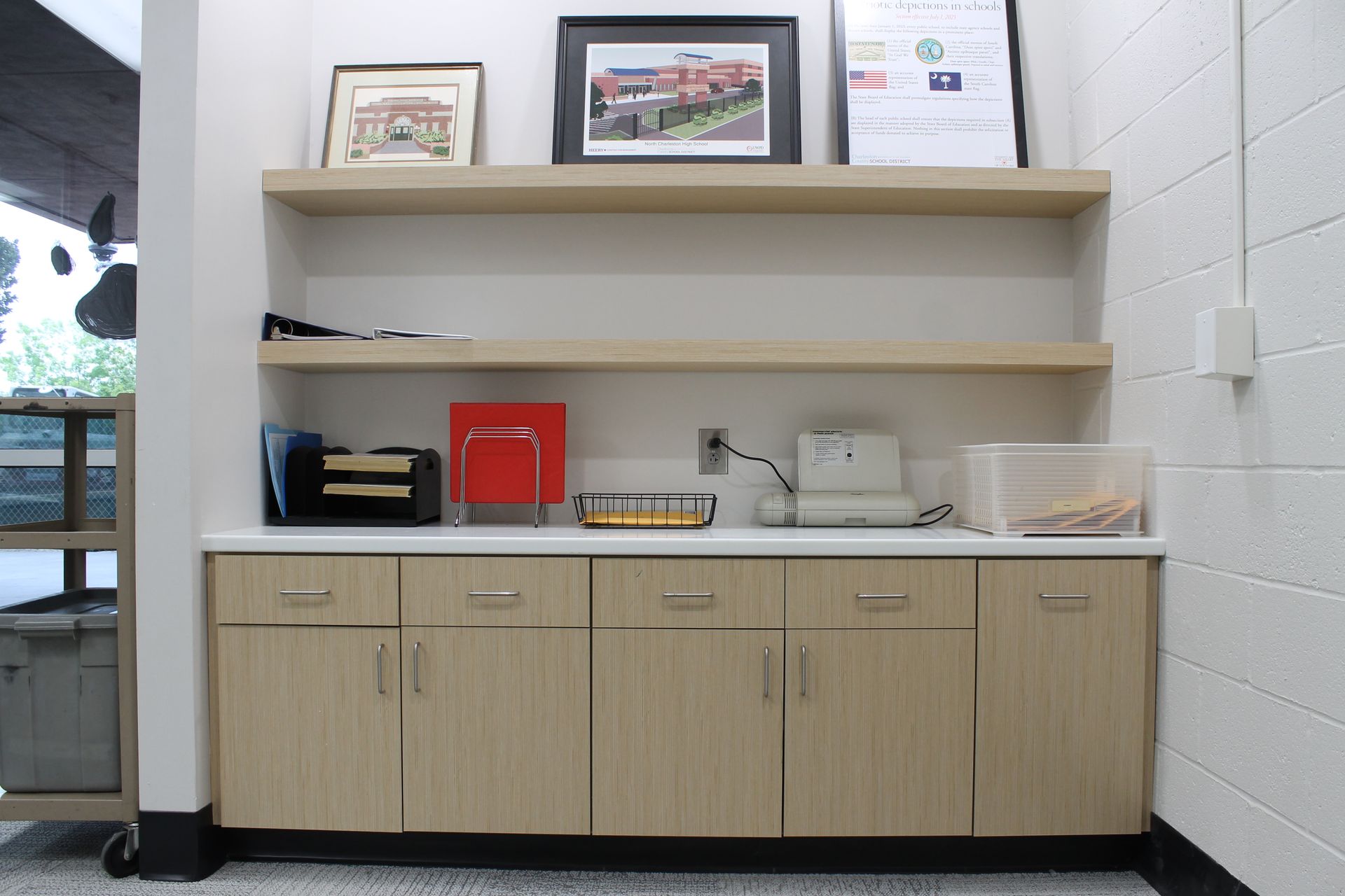 A built-in counter and cabinets with shelves above. Contains desk items and framed pictures.