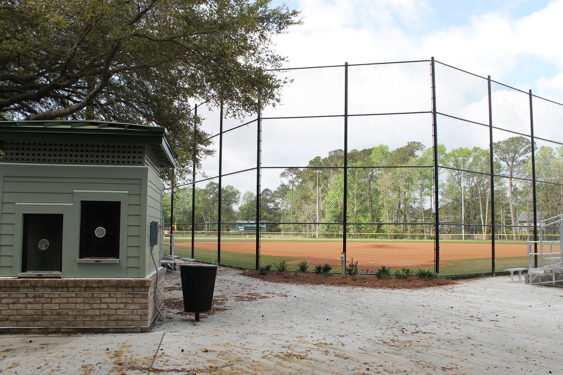 Baseball field with a chain link fence, dugout, and trees in the background.
