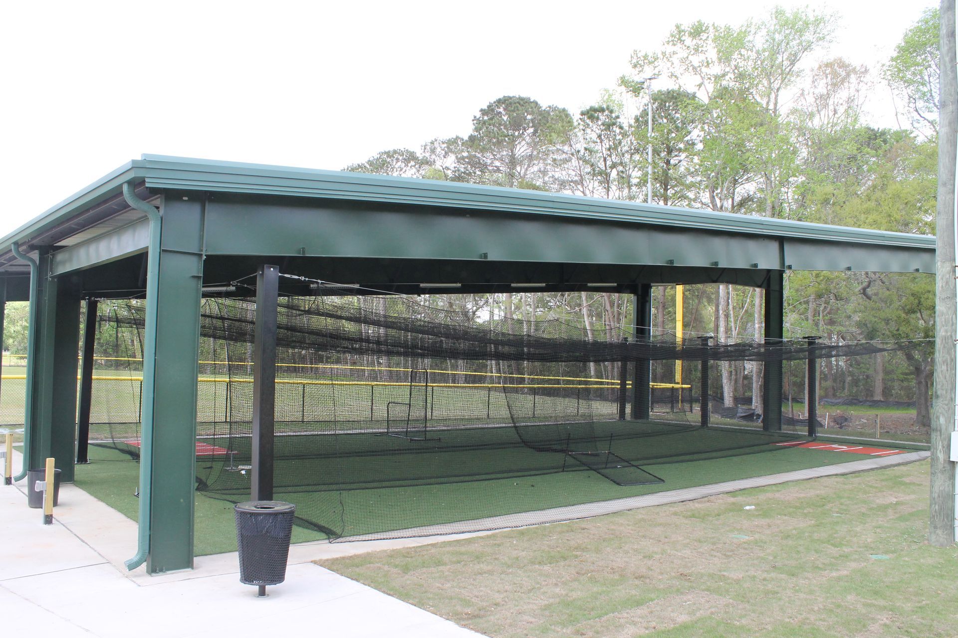 Baseball batting cage with green roof and netting, set on artificial turf.