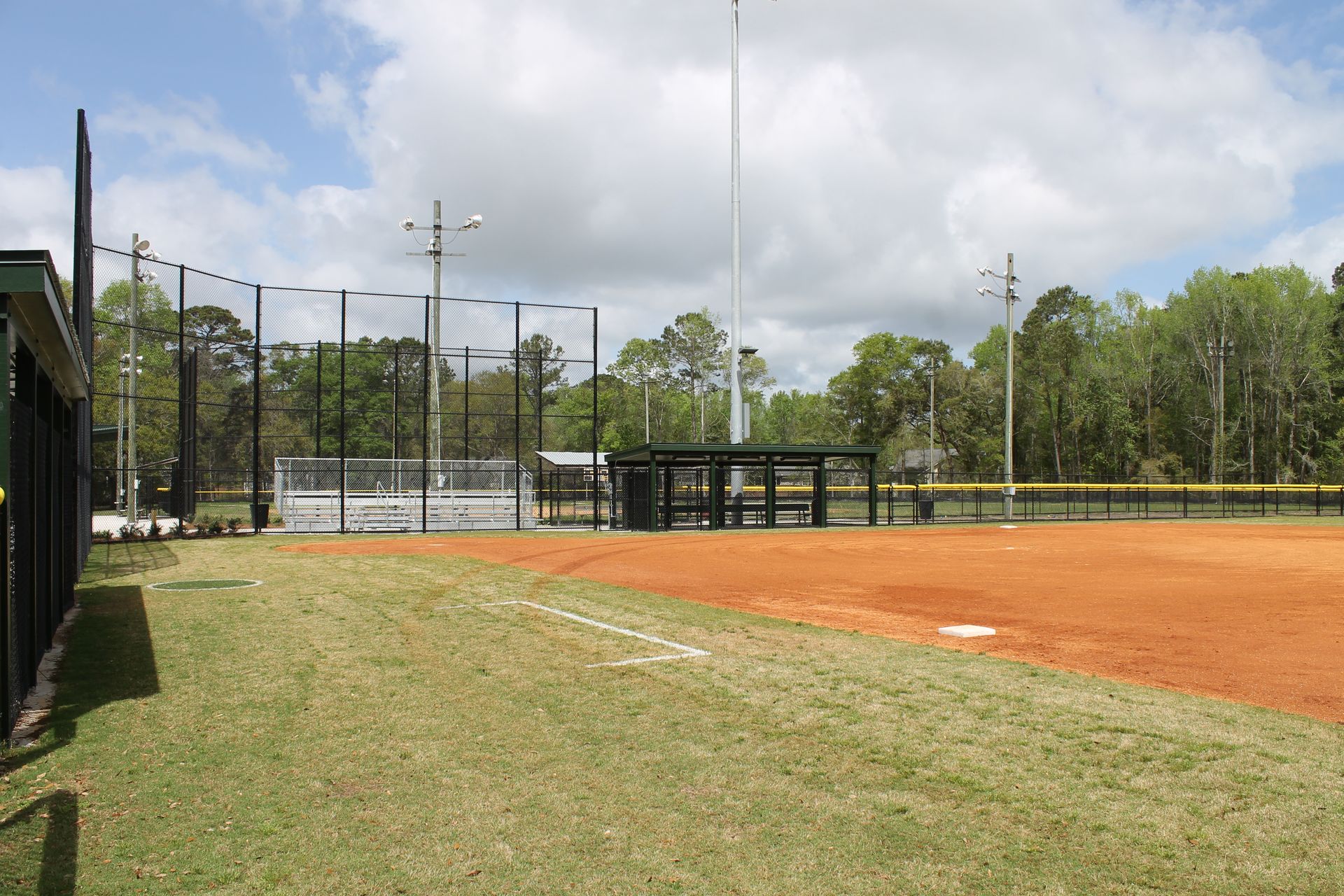 Softball field with red dirt infield, green outfield, and covered dugout.
