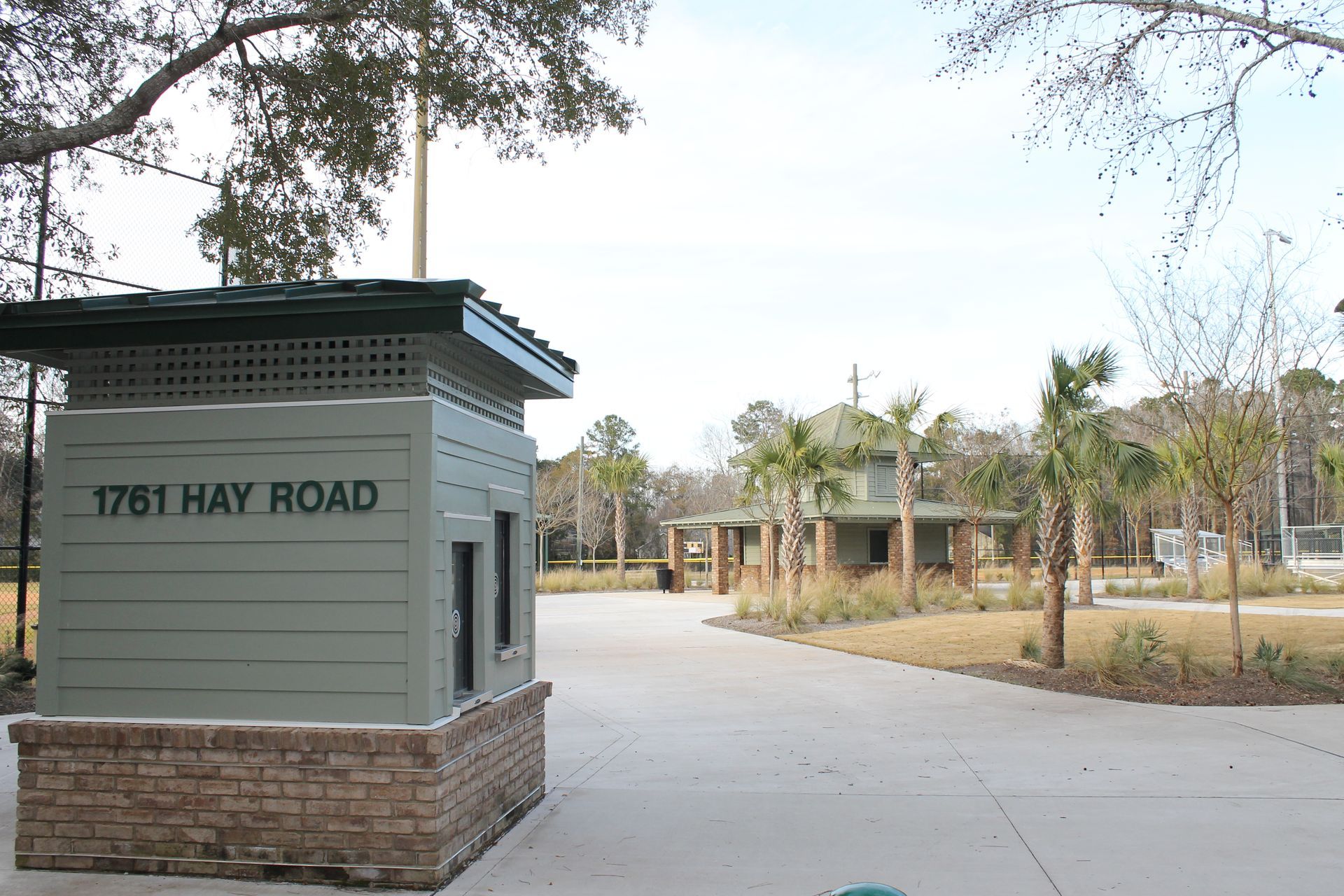 Entrance kiosk at 1761 Hay Road. Green structure with sign, brick base. Palm trees and grassy area visible.
