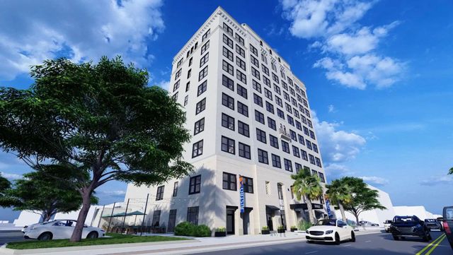 Tall white building on a sunny day with trees and cars on a street.