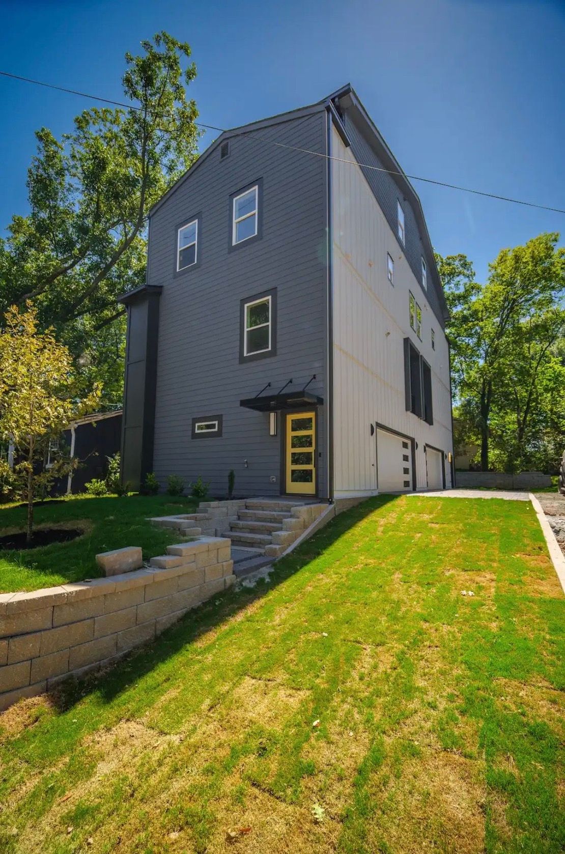 Modern gray house with yellow front door, three stories, and a sloped green lawn.