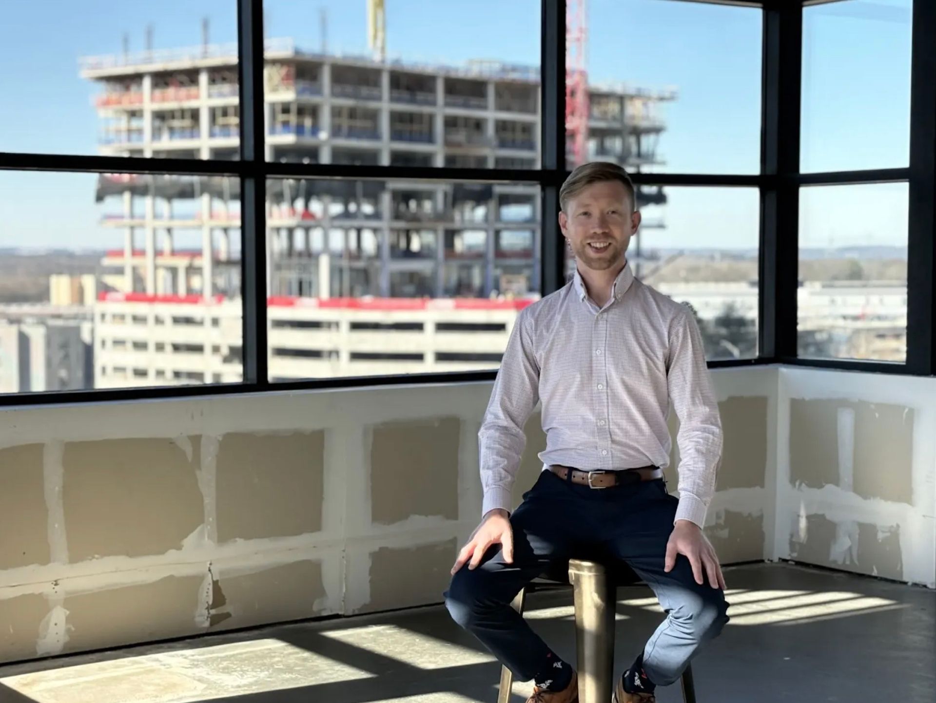Man sitting, smiling, near window overlooking construction site.