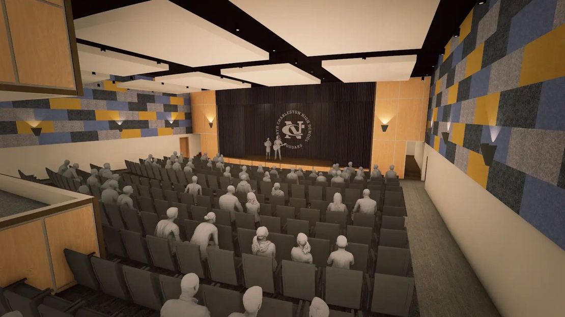 Auditorium with rows of seats facing a stage with figures on it. Walls have blue and yellow accents.