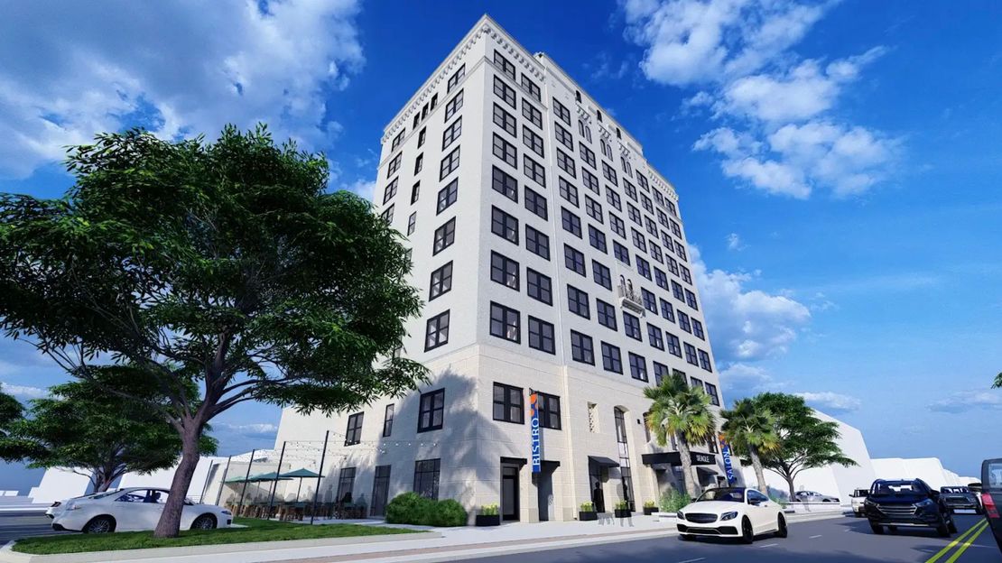 Tall white building on a sunny day with cars on the road and trees lining the street.