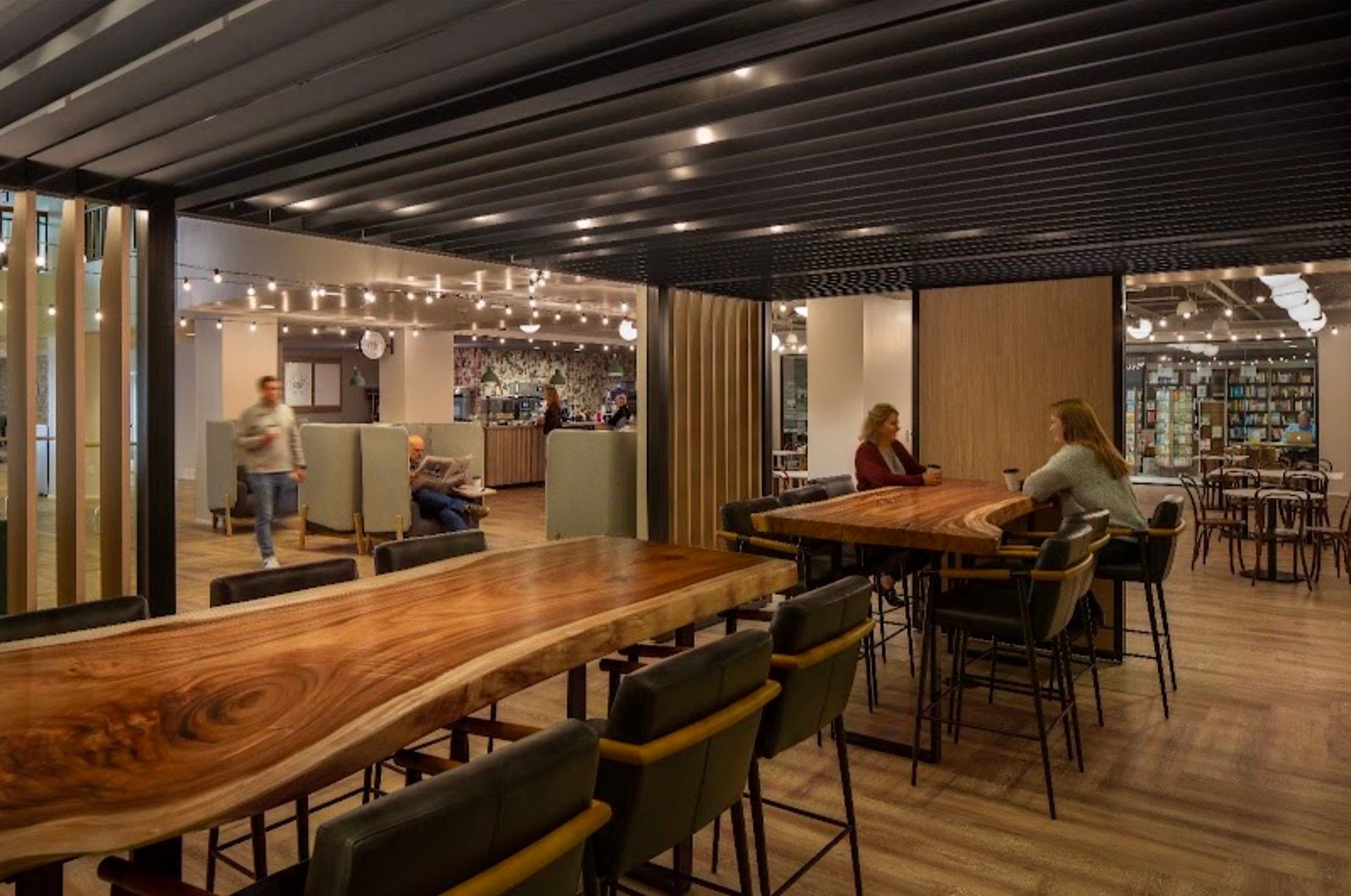 Modern office space with wooden tables, chairs, and people working.