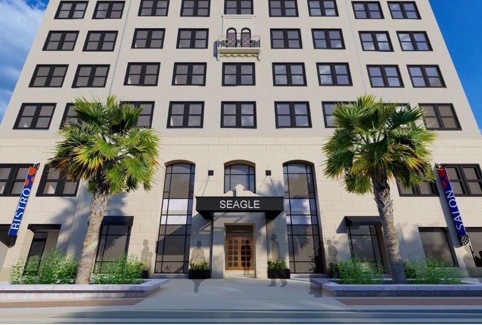 Exterior of the Seagle building with palm trees and a light beige facade, entrance under a black awning.