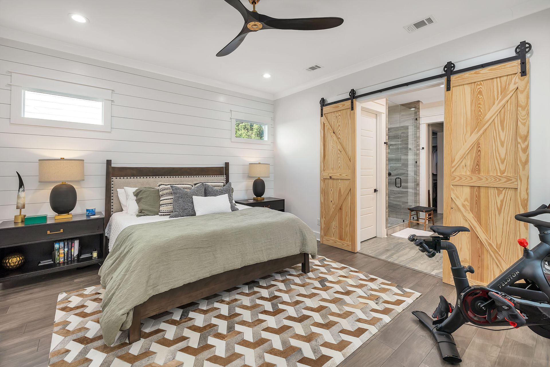 Bedroom with bed, barn doors to bathroom, exercise bike, and patterned rug.