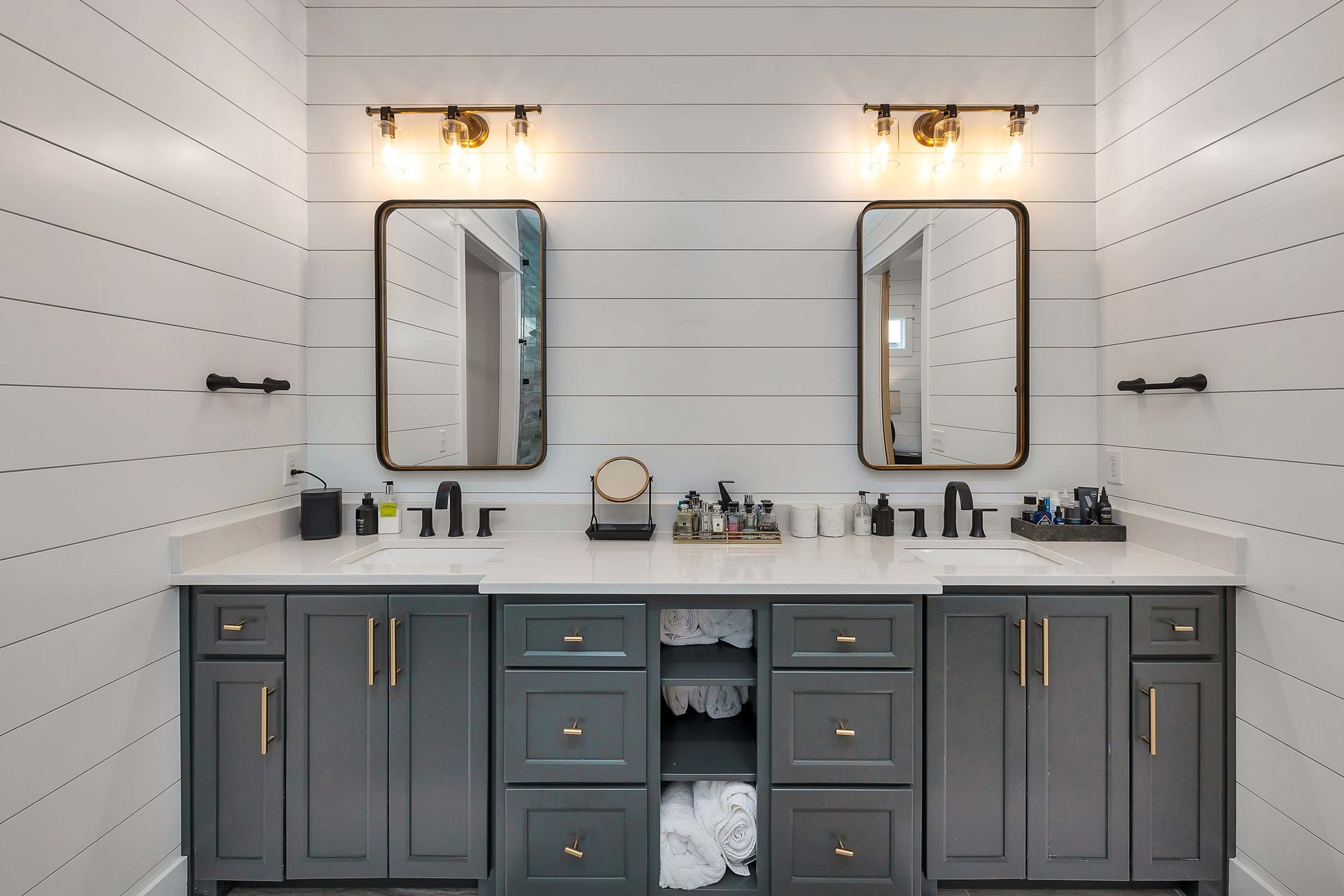 Bathroom with gray cabinets, white countertop, two mirrors, and shiplap walls.