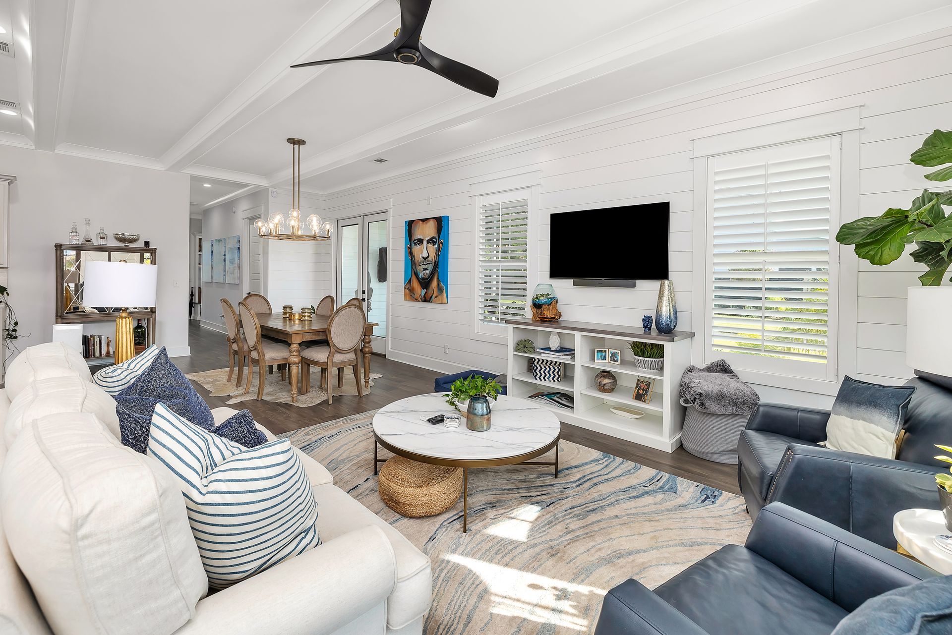 Spacious living room with white walls, blue furniture, a large TV, and a dining area visible.