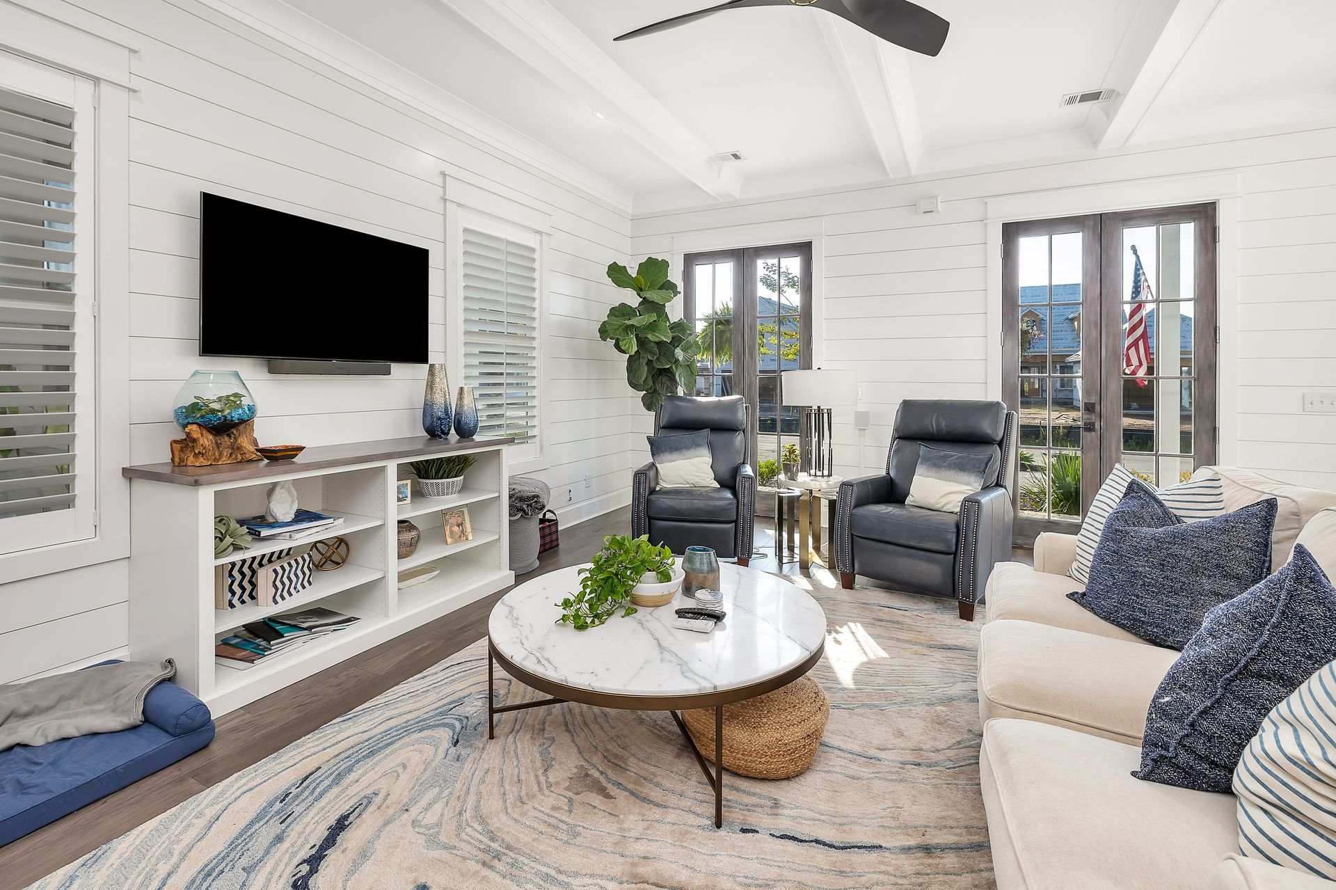 Living room with white shiplap walls, TV, cream sofa, marble coffee table, and blue recliner chairs.