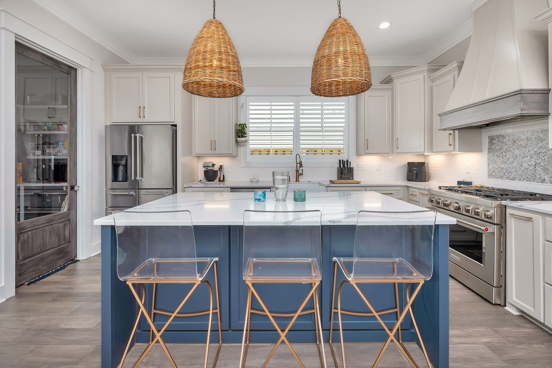 Modern kitchen with blue island, clear bar stools, and wicker pendant lights.