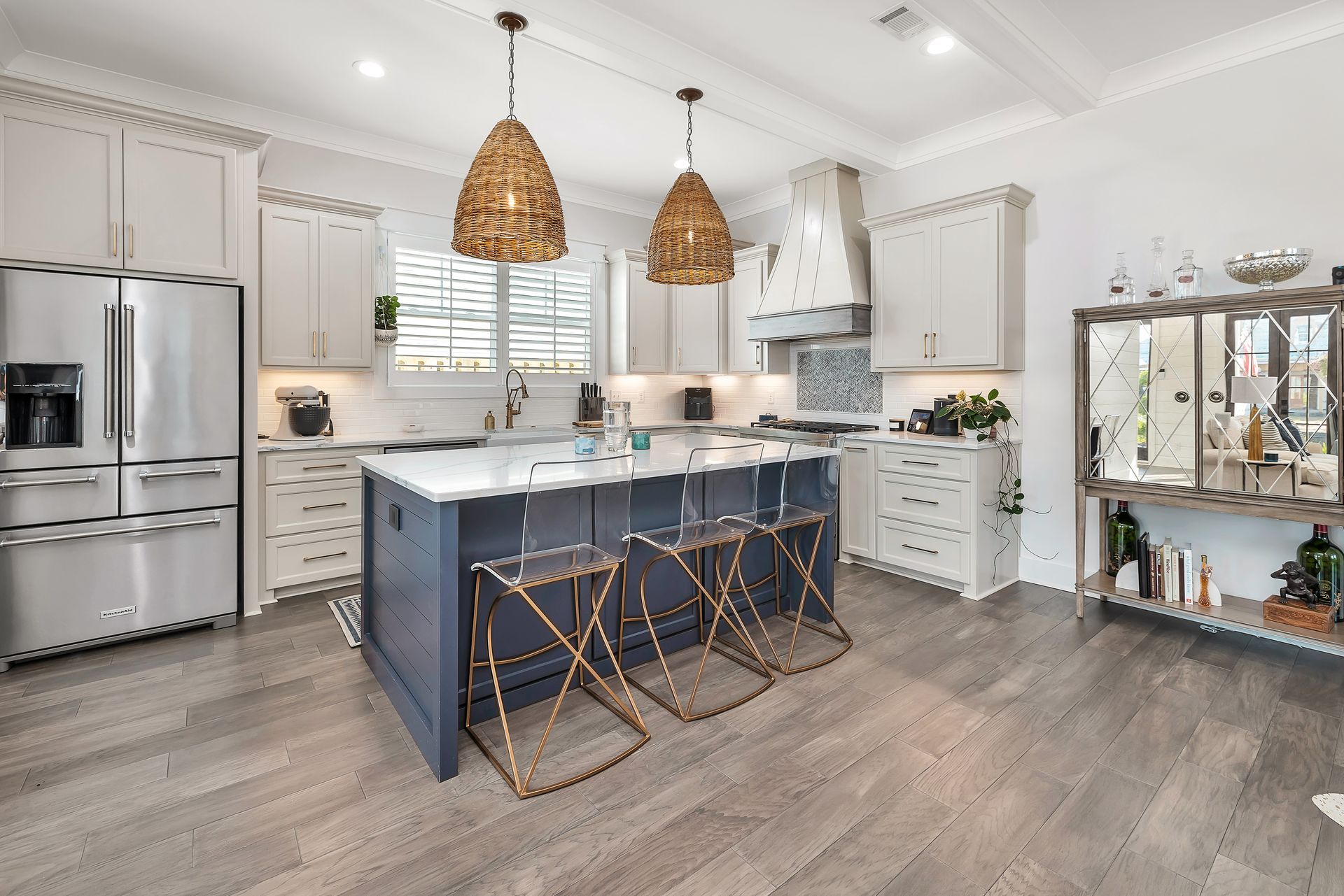 Modern kitchen with white cabinets, blue island, woven pendant lights, and stainless steel appliances.