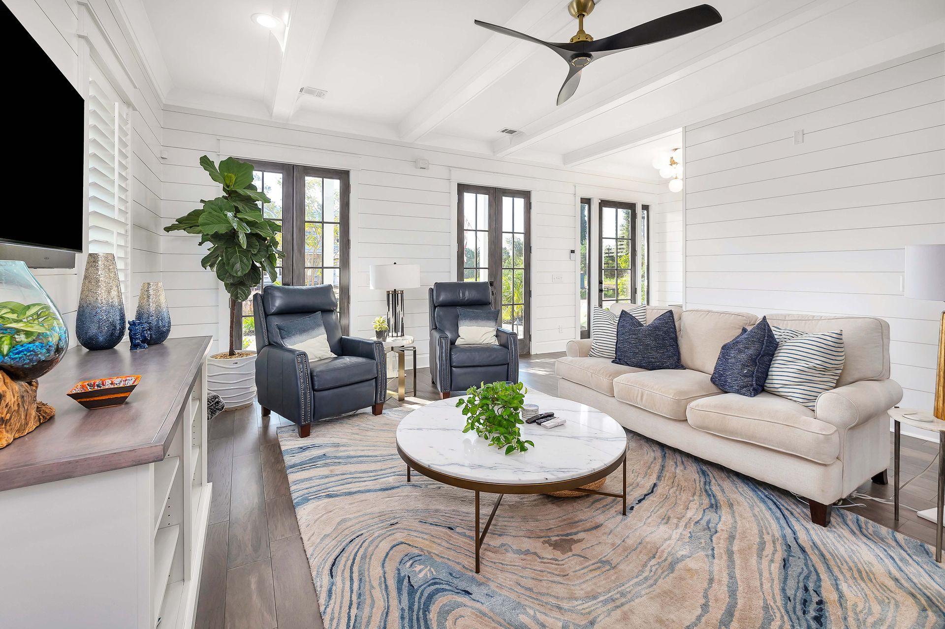 Living room with blue accents: sofa, armchairs, marble coffee table, patterned rug, TV.