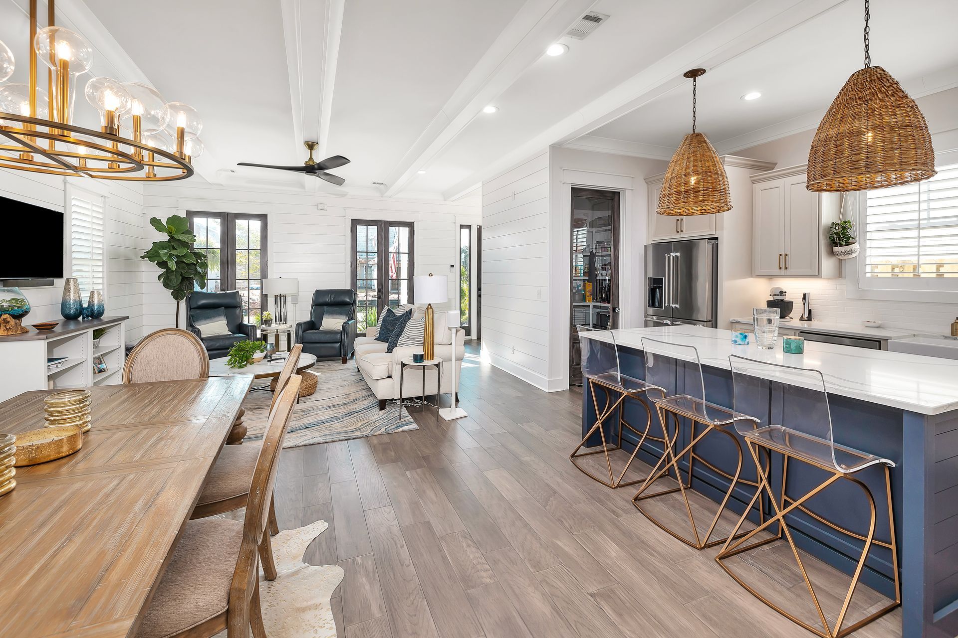 Open-concept living space with kitchen, dining, and living areas. Blue island, wooden floor, neutral colors.