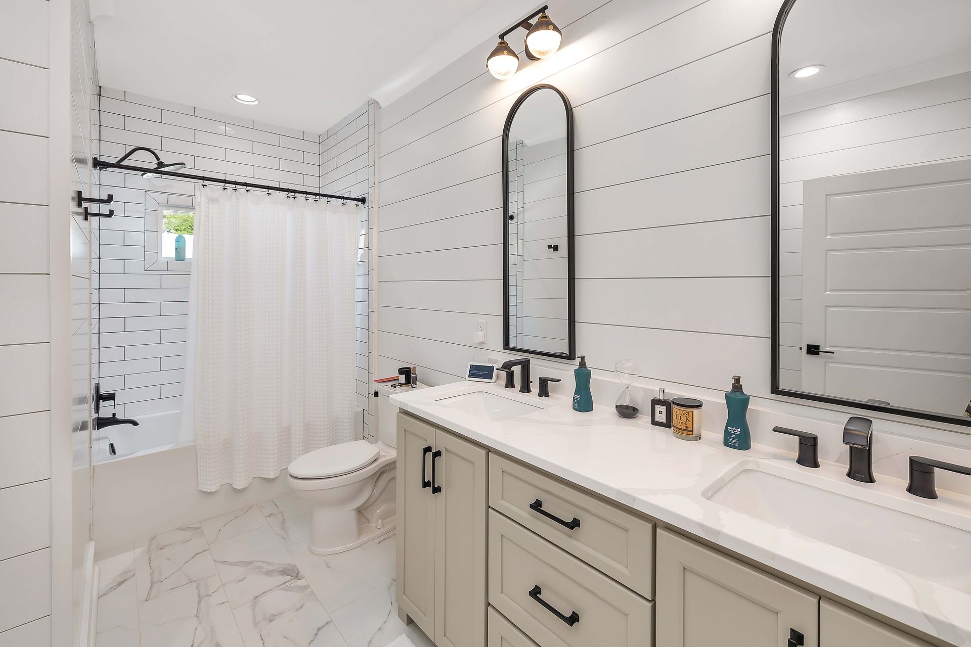 White bathroom with dual vanity, black fixtures, and a shower/tub.