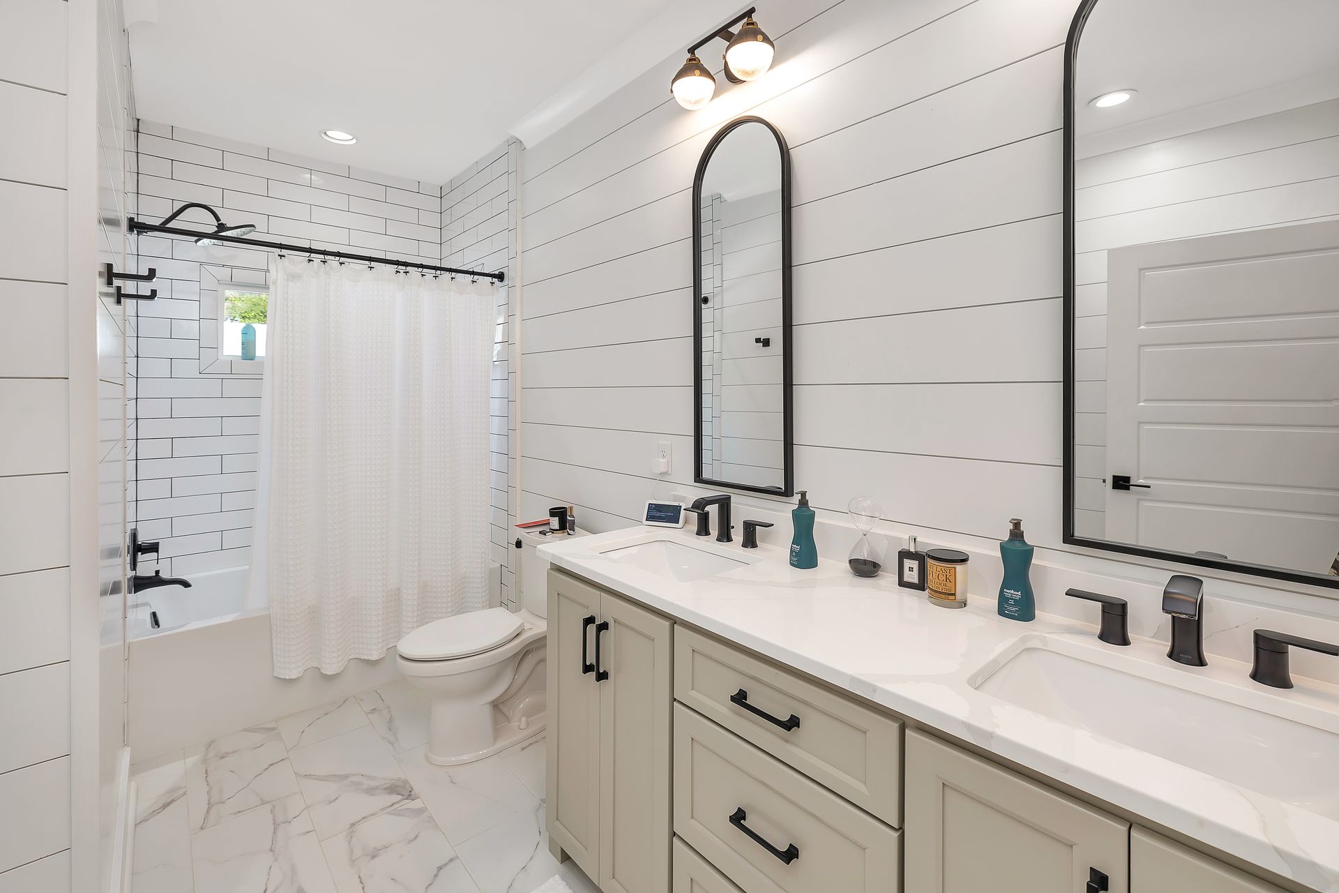 Bright, modern bathroom with white shiplap walls, double vanity, arched mirror, and black fixtures.