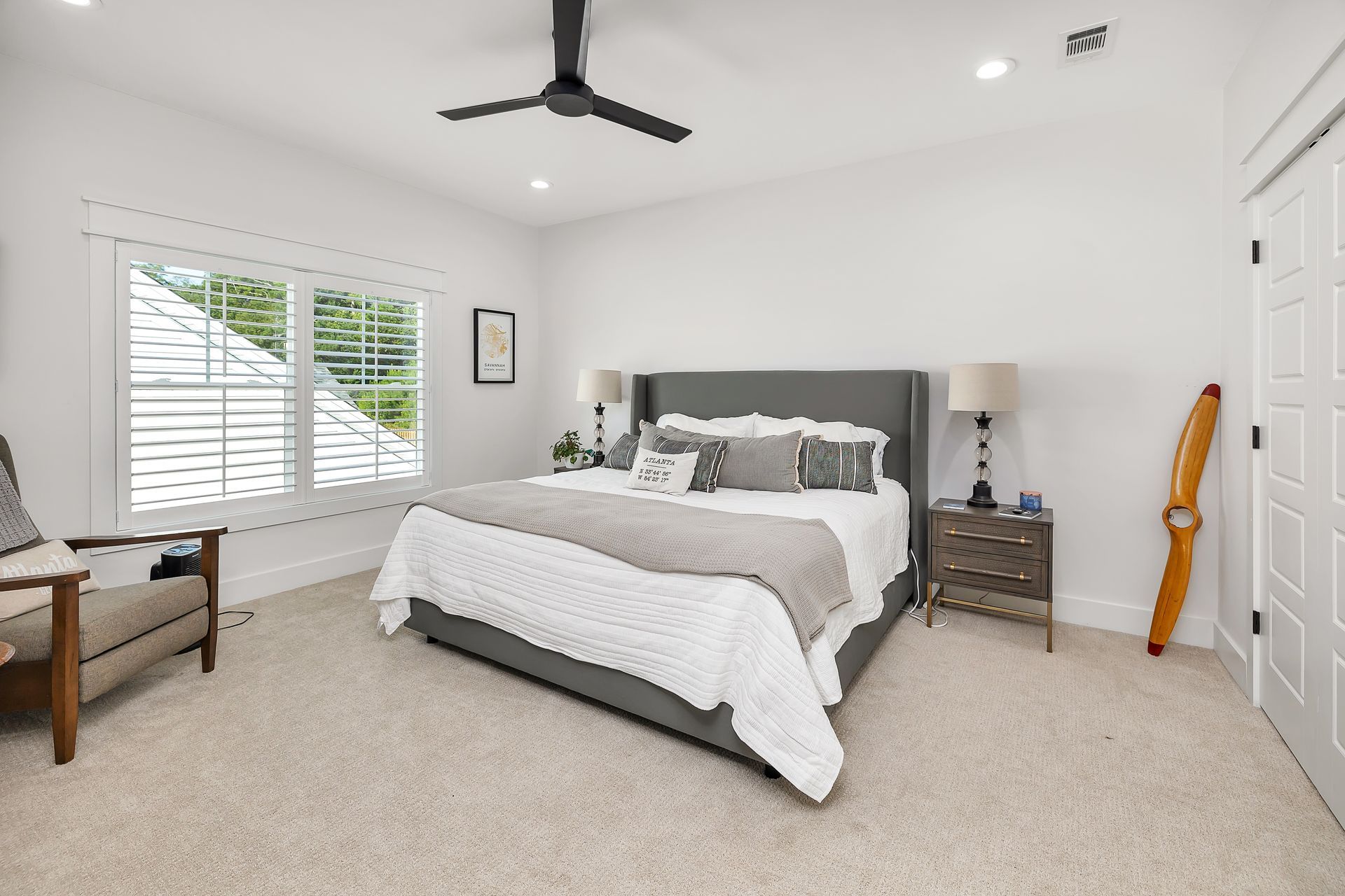 Bedroom with a gray bed, white walls, carpet, window, ceiling fan, and a wood chair.