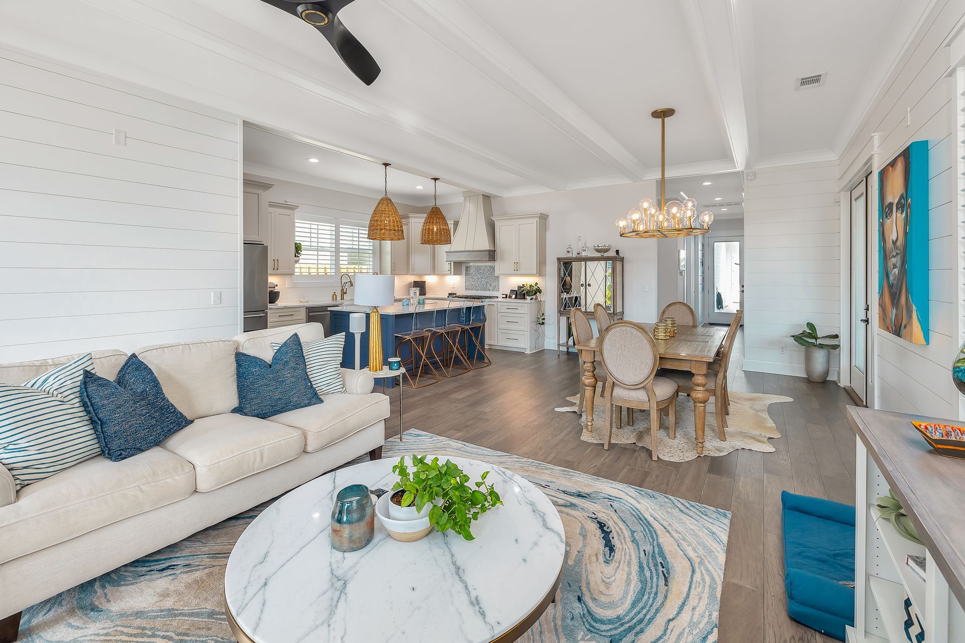 Open-concept living space with kitchen, dining area, and seating. Neutral tones, blue accents, light wood flooring.