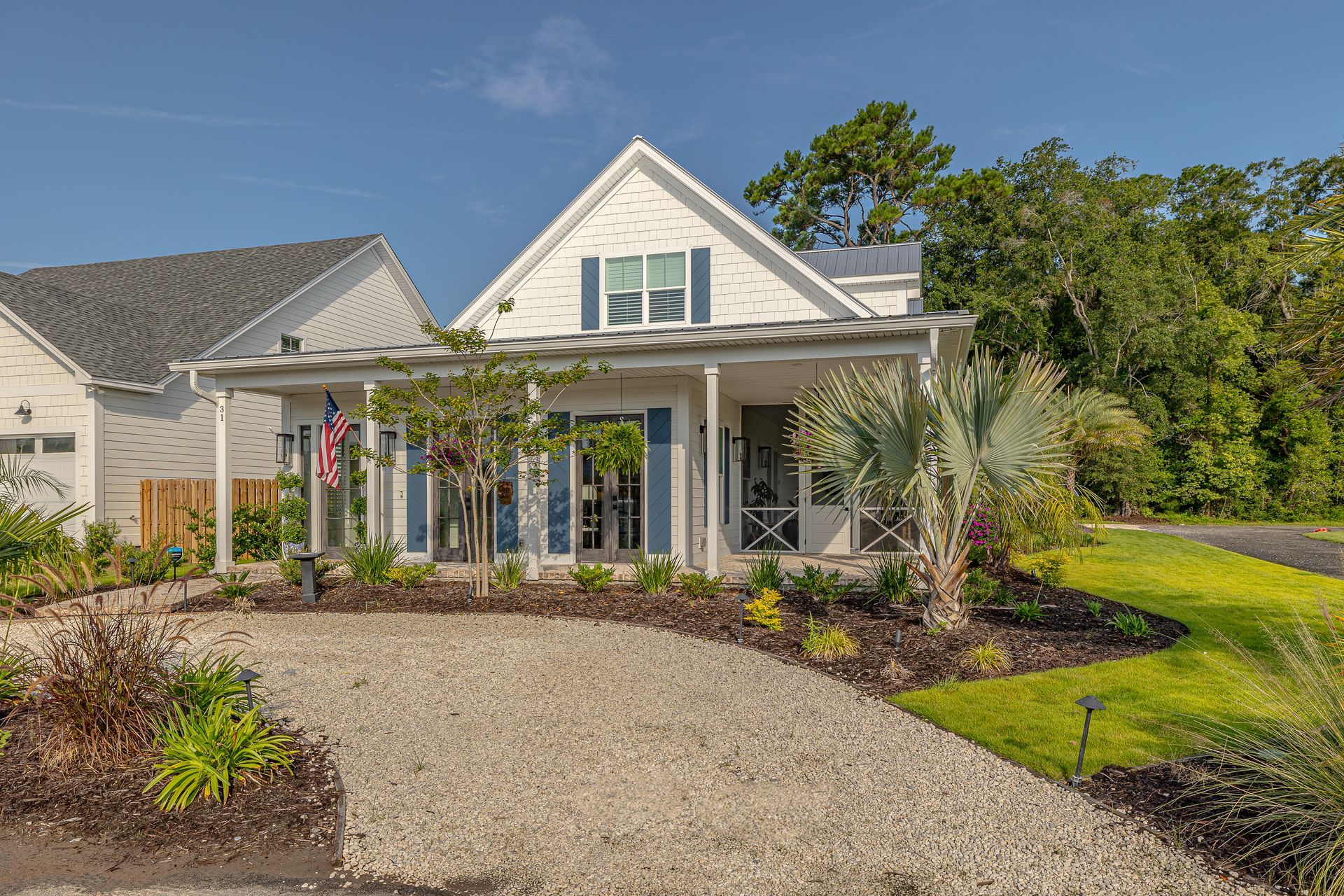 White cottage with blue shutters, covered porch, gravel driveway, and landscaped yard.