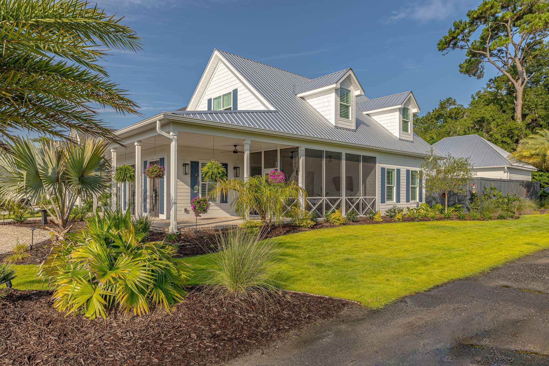 White cottage with screened porch, metal roof, green shutters, and manicured lawn.