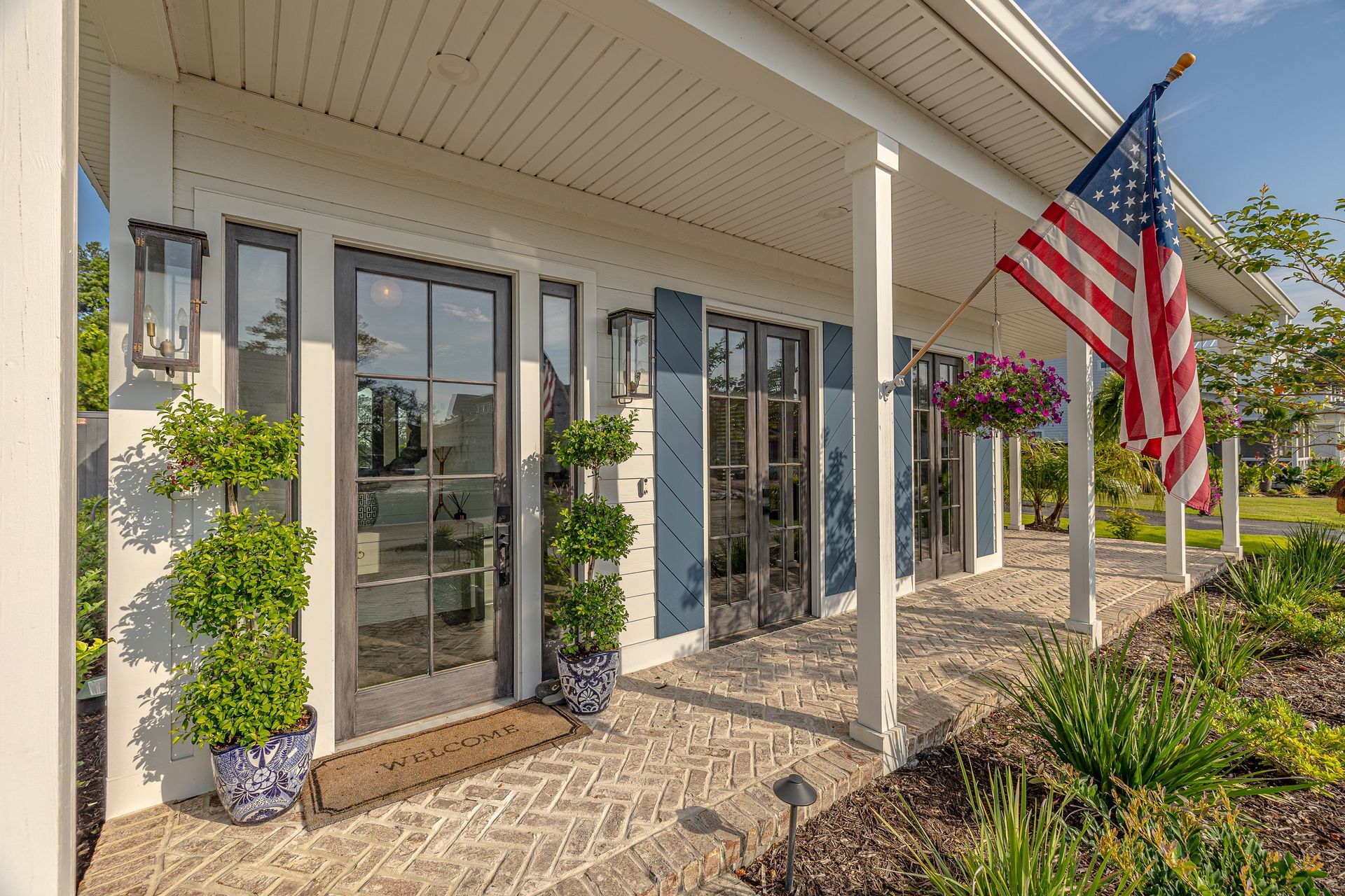 White house with glass doors, blue shutters, and American flag on the porch.