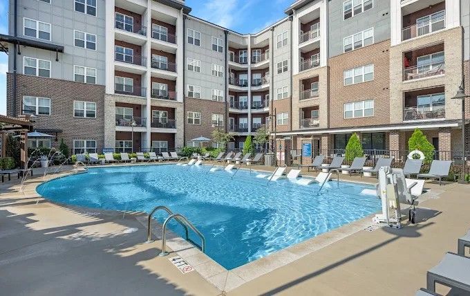 Aerial view of a pool with lounge chairs, blue umbrellas, and a shaded seating area.