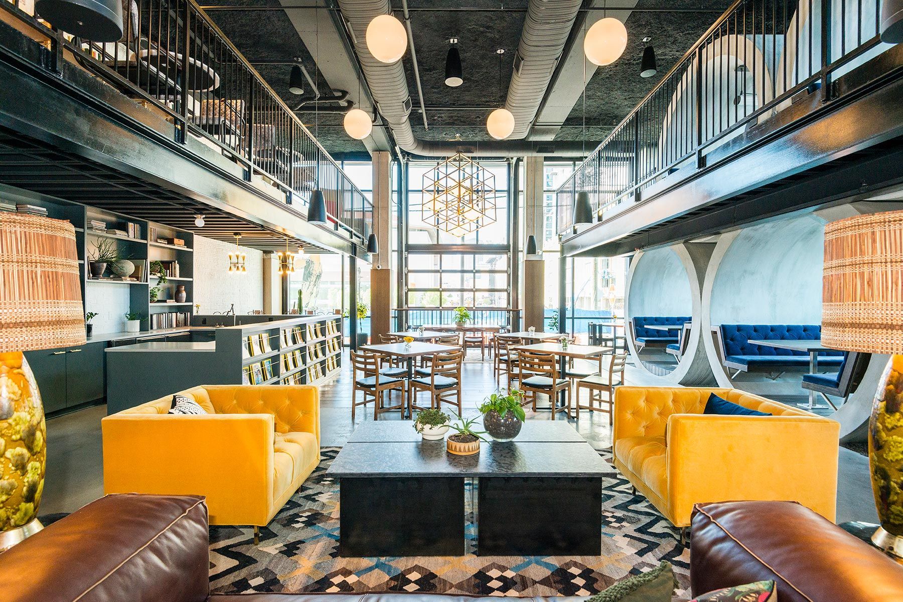 Lounge area with yellow sofas, dark gray coffee table, and tables with chairs. The setting has a modern design.