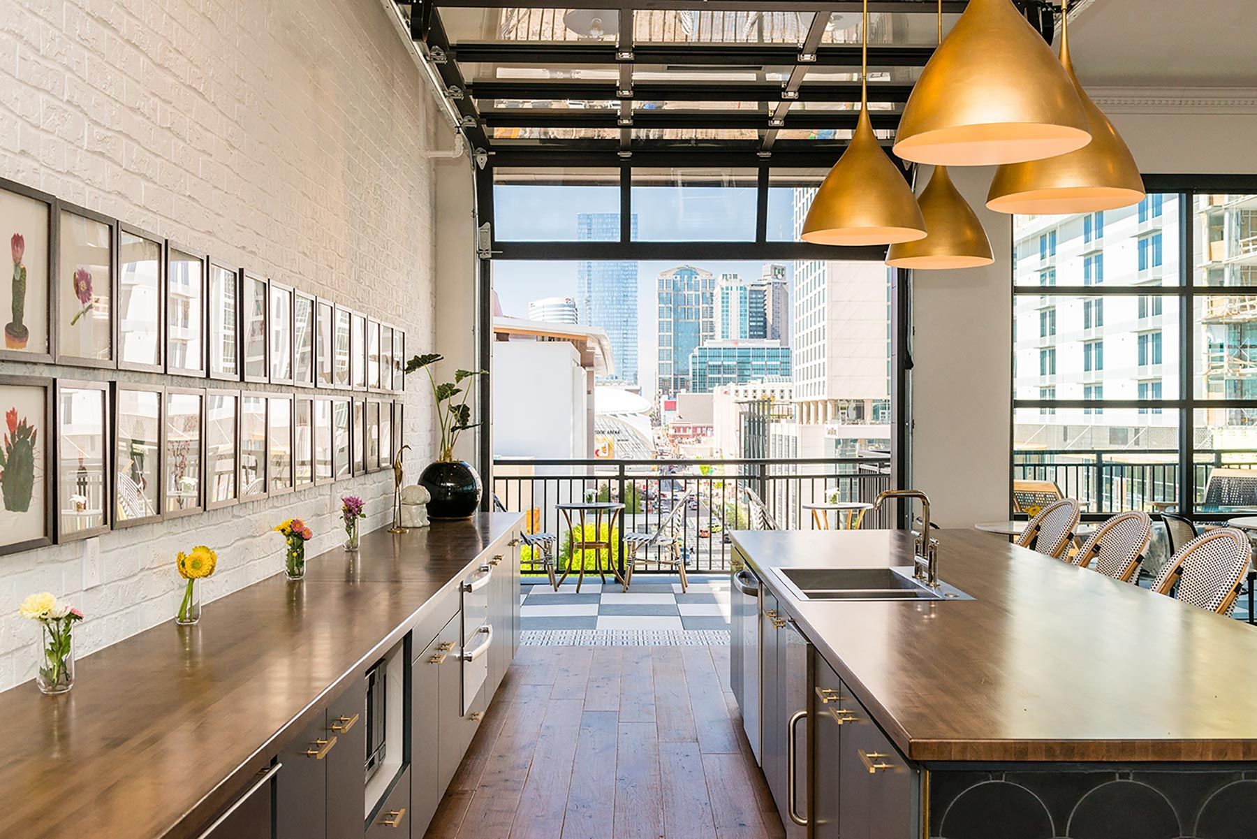 Modern kitchen with long wooden counters, gold pendant lights, and city view.