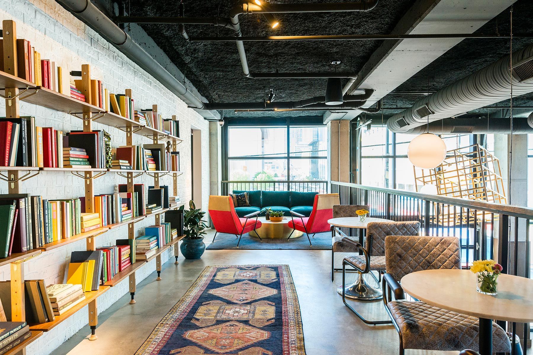 Interior with bookshelves, seating area with sofa, chairs, rug, and round tables near windows.