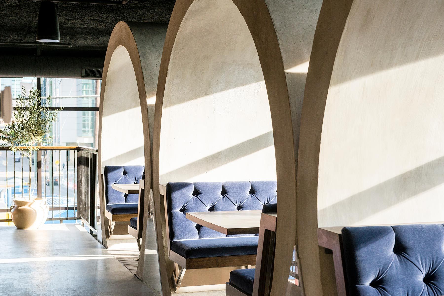 Restaurant booth seating with arched dividers, navy blue upholstery, and a sunny, modern setting.