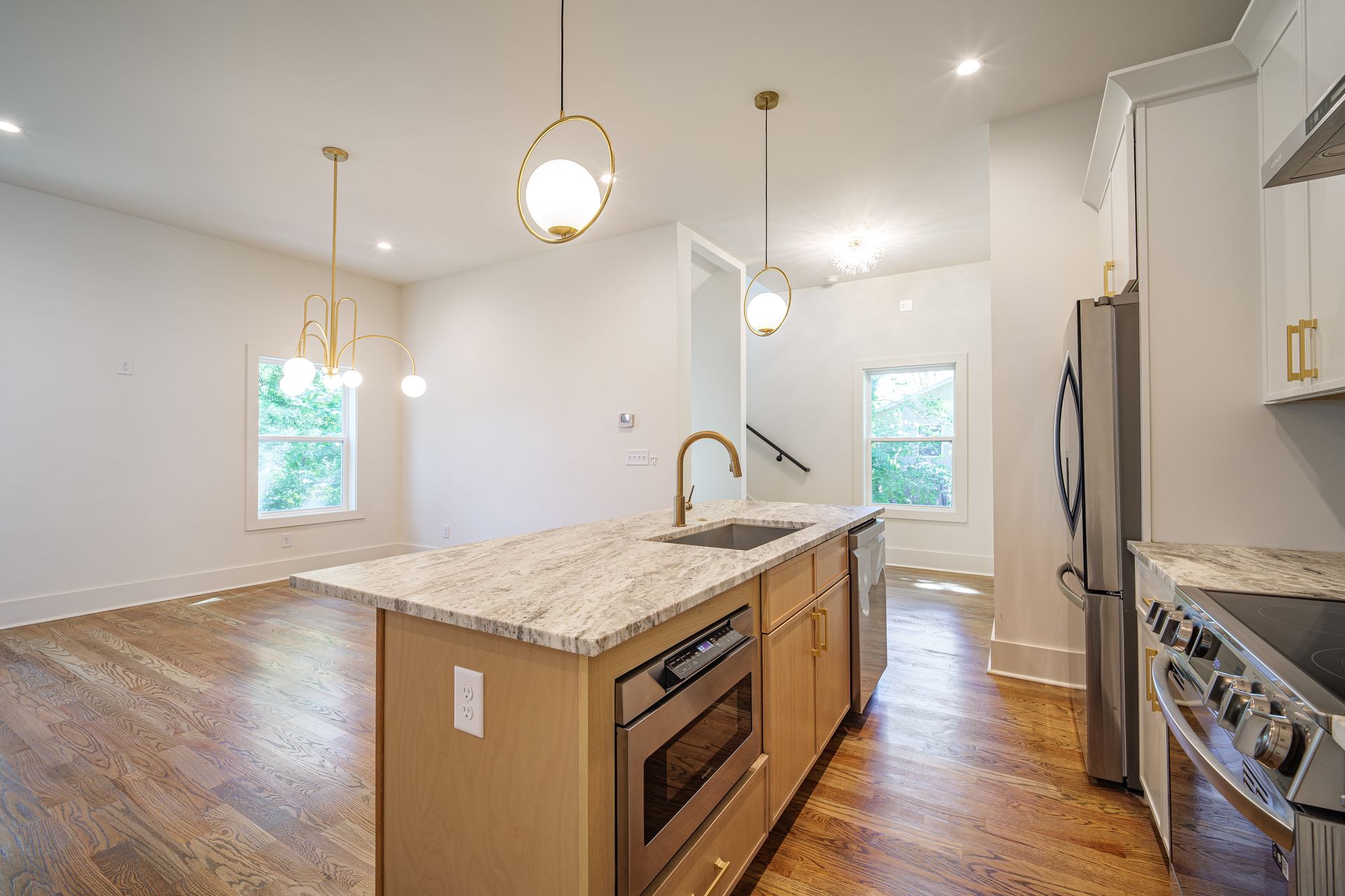 Kitchen with island, granite counters, stainless appliances, gold pendant lights, and hardwood floors.