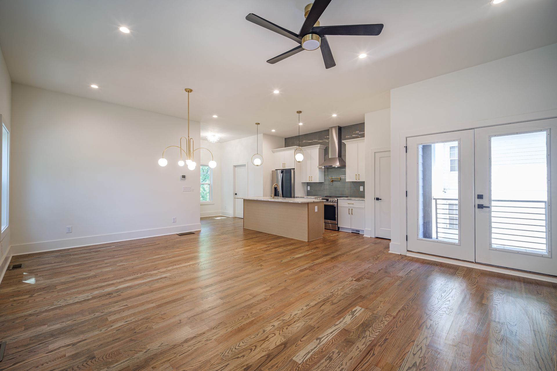 Bright, open-concept living space with hardwood floors, a kitchen island, and French doors to a balcony.