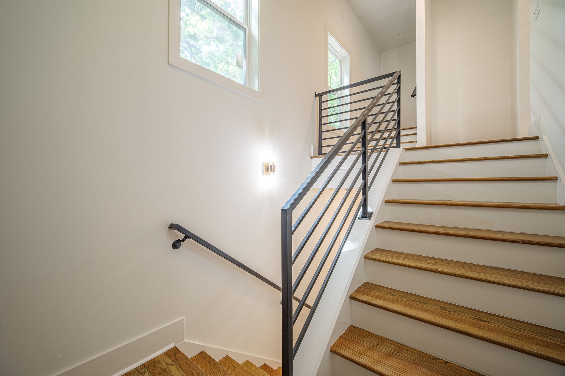 Staircase with wooden steps and modern metal railing. Off-white walls and windows.