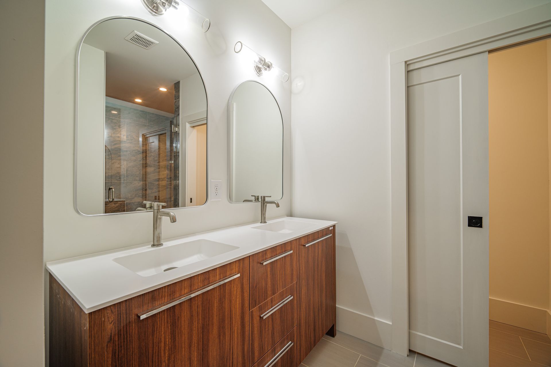 Modern bathroom with double vanity, arched mirrors, and a sliding door.