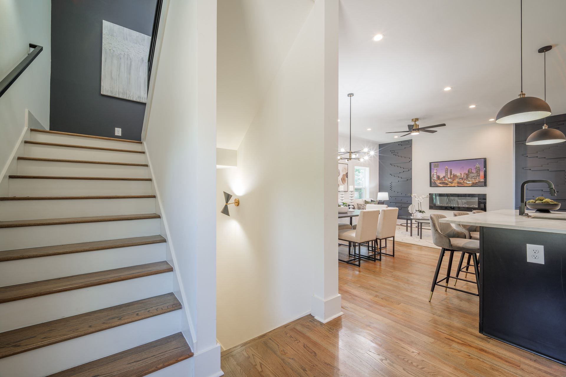 Staircase leads to open-concept living space with hardwood floors, dark accent wall, and kitchen island with pendant lights.