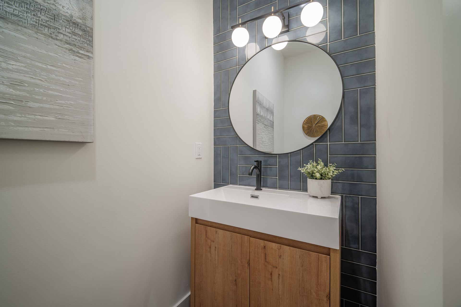 Bathroom with wood vanity, round mirror, blue tiled wall, and white countertop.