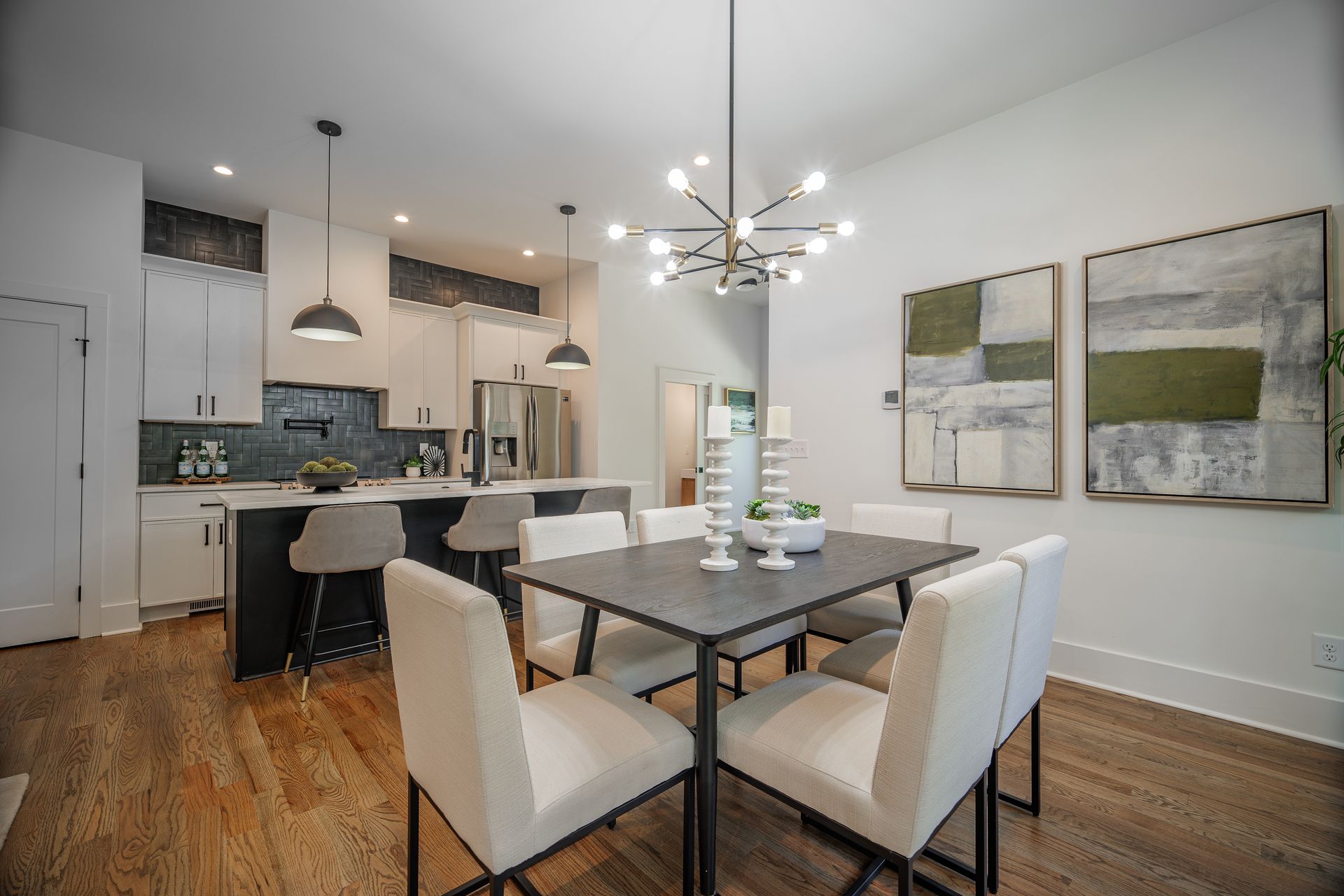Dining room with table and chairs, adjacent to kitchen with white cabinets, and artwork on wall.