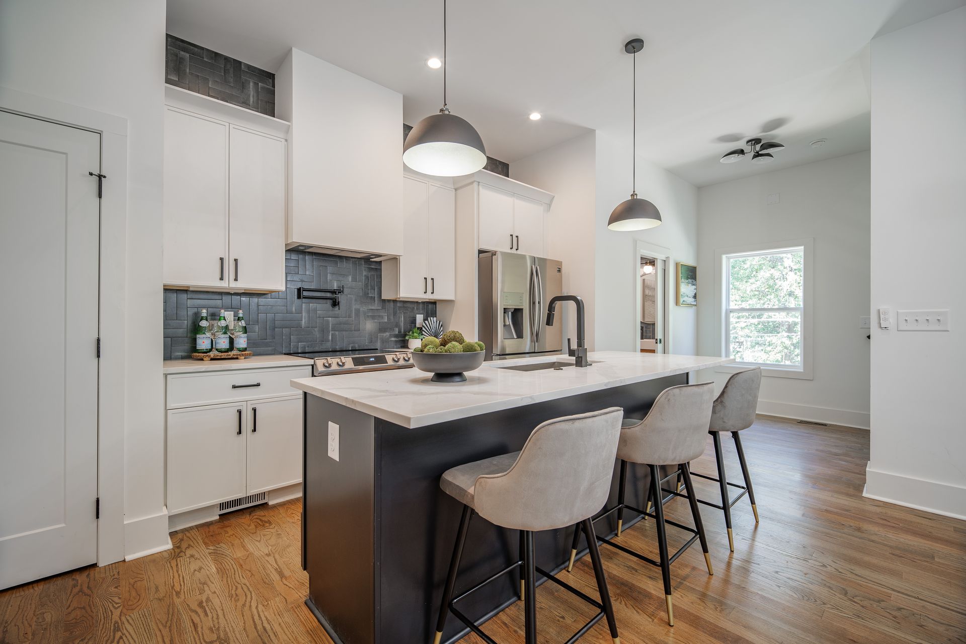 Modern kitchen with white cabinets, dark island with seating, hardwood floors, and overhead lighting.