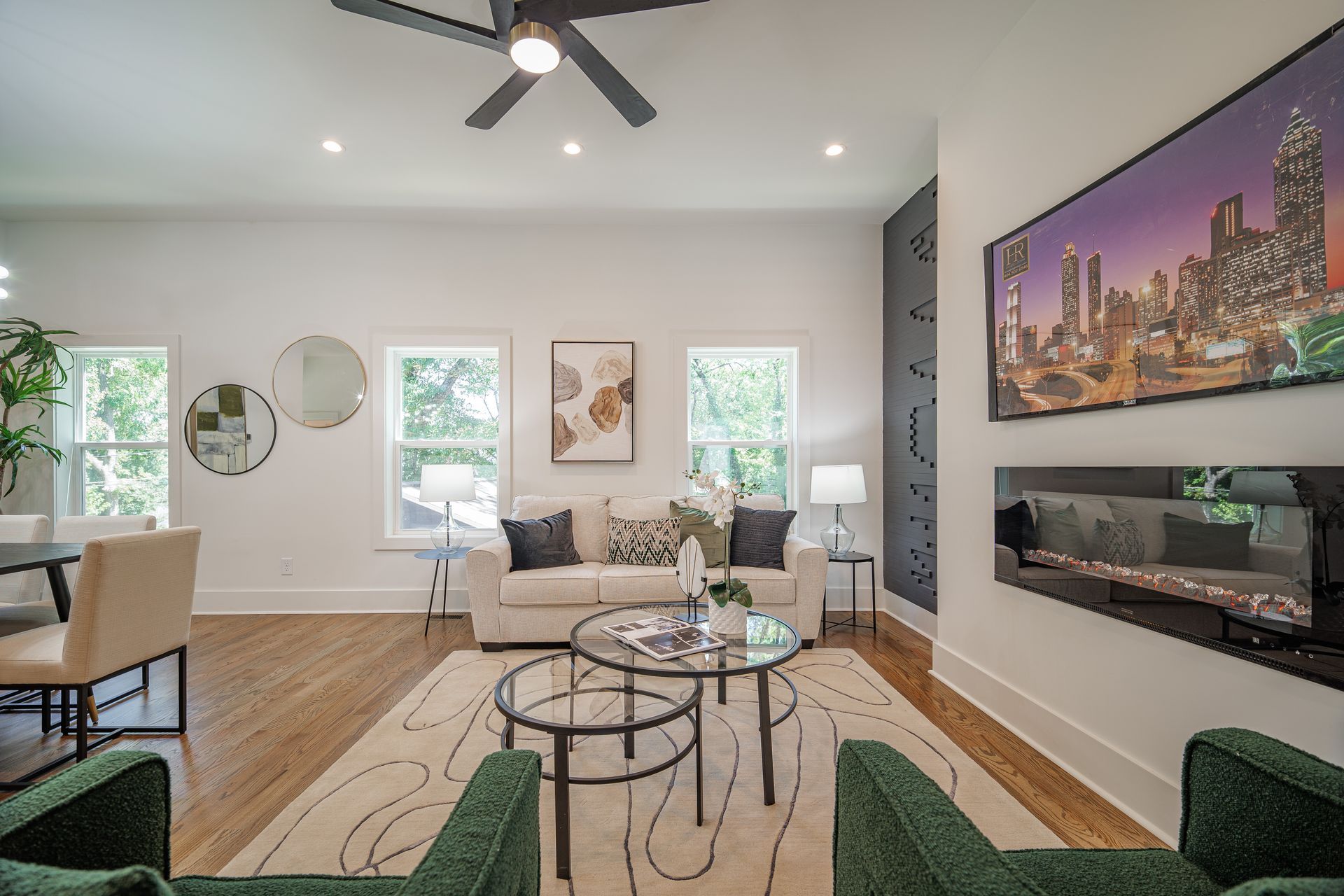 Living room with sofa, green chairs, fireplace, artwork, and windows.